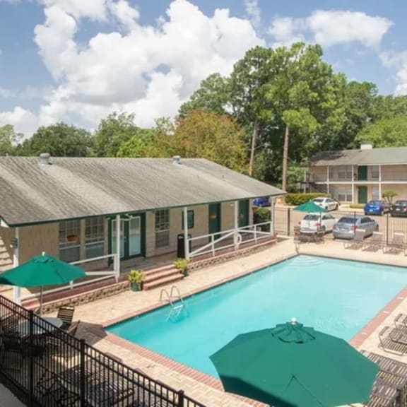 a pool surrounded by a black fence with green umbrellas.