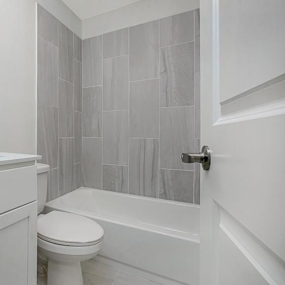 a white bathroom with a toilet, sink, and tiled shower.