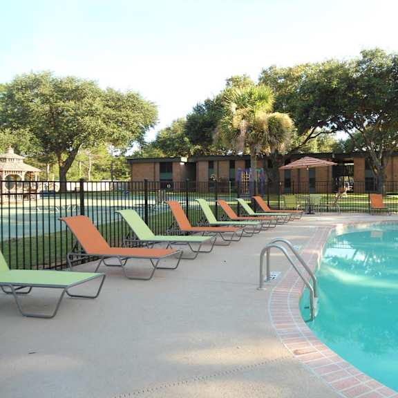 a pool with a metal fence and orange and green lounge chairs.