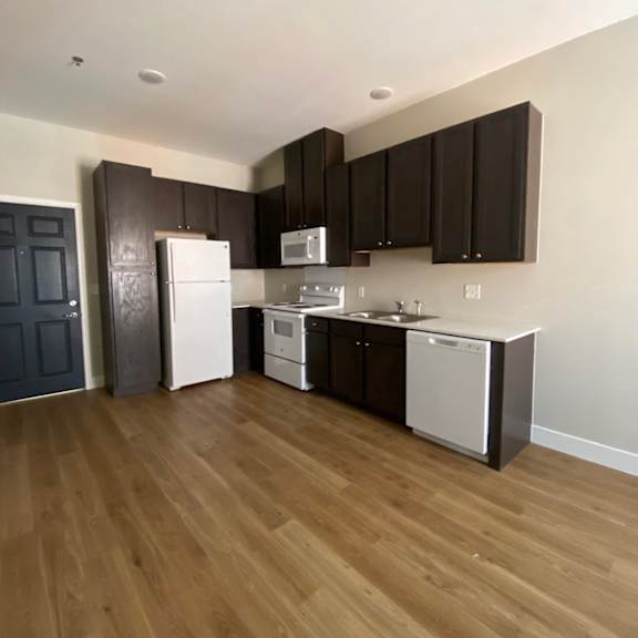 an empty kitchen with black cabinets and white appliances and wood floors