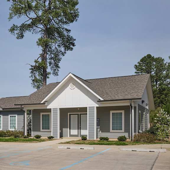 a small building with a grey roof and a parking lot in front.