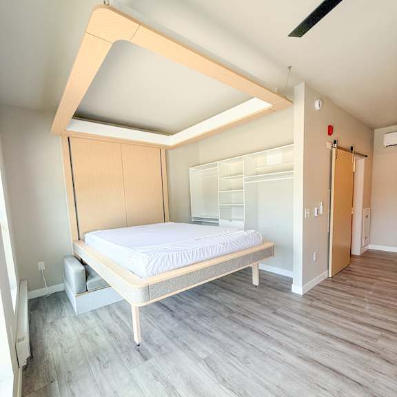 a bed with a wooden frame and mattress is in a room with a wooden floor and a ceiling with a skylight.