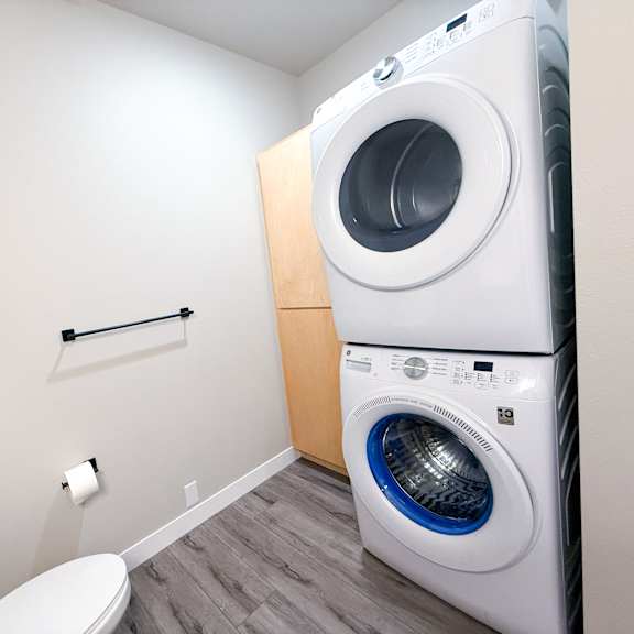 a white washing machine sits in a laundry room next to a toilet.