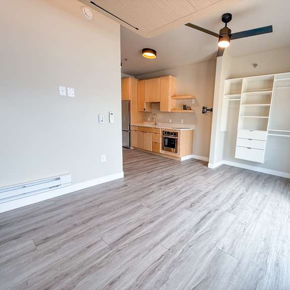 a room with a ceiling fan and a kitchen area in the background.