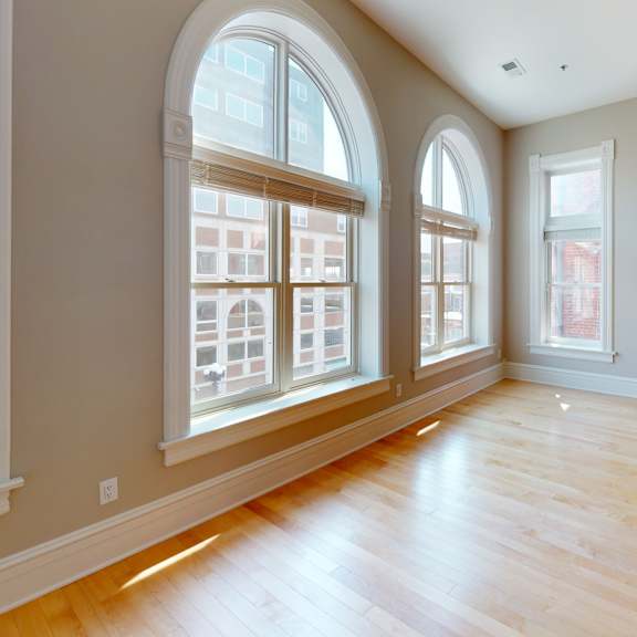 an empty living room with three large windows and wood floors