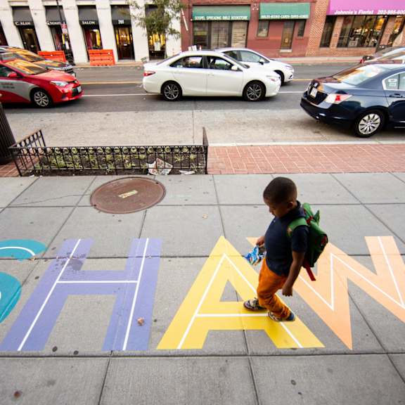 a boy walking on a sidewalk with the letters shan spray painted on it.