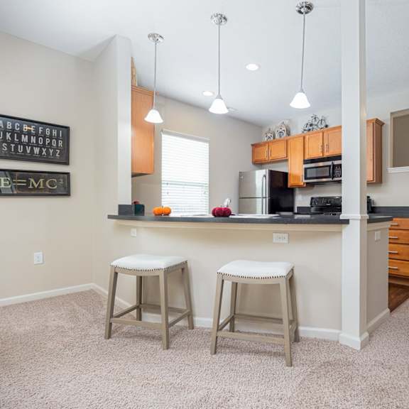 a kitchen with white walls and a white ceiling with a fridge, stove and bar stools.
