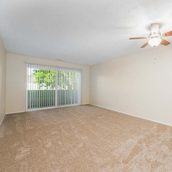 an empty living room with a ceiling fan and a window