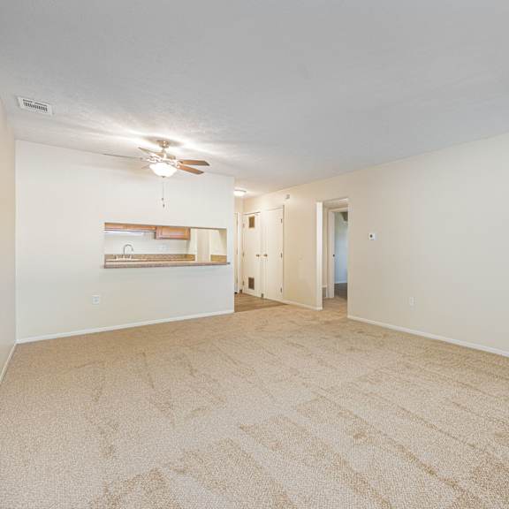 a spacious living room with carpet and a ceiling fan