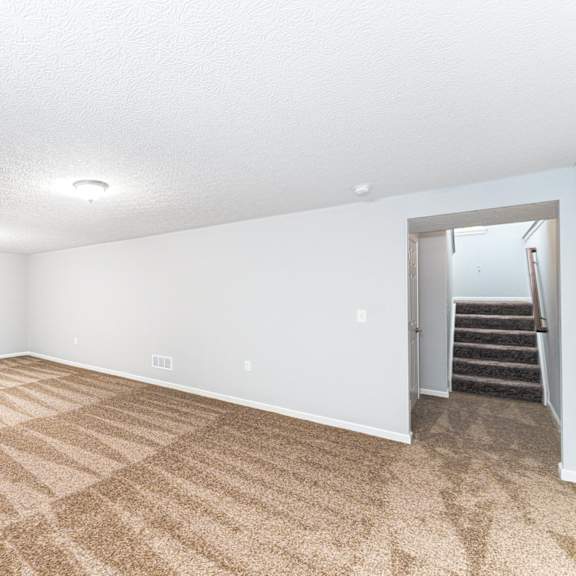 a room with a carpeted floor and a staircase in the background.