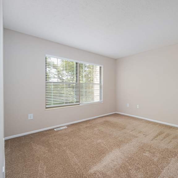 an empty living room with a window and carpeting