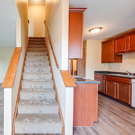 an empty living room with stairs leading up to a kitchen
