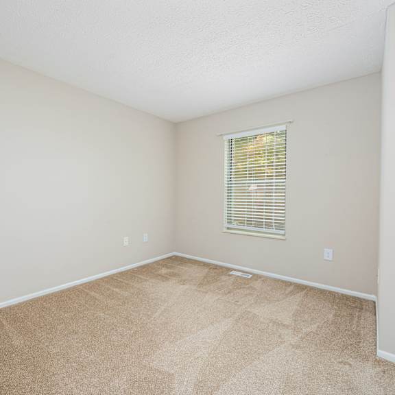 an empty room with a window and beige carpet
