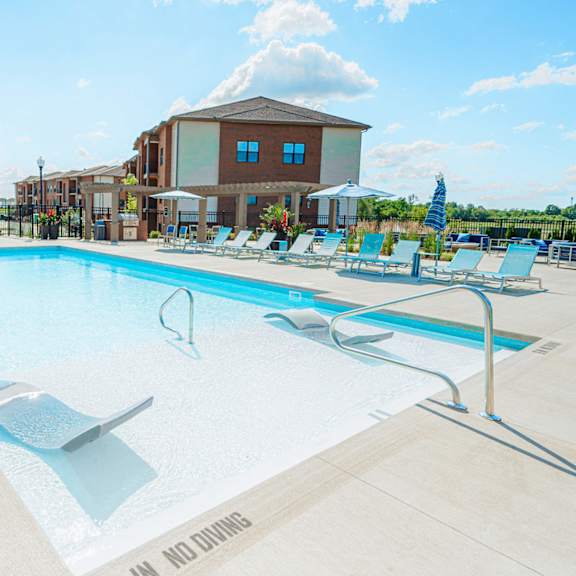 a swimming pool with chairs and a building in the background