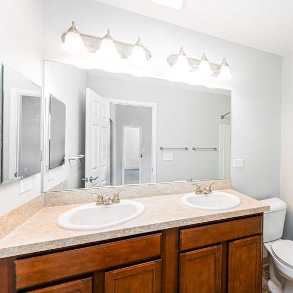 a white bathroom with a double sink and a toilet.