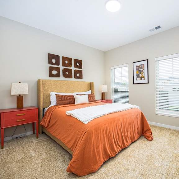 a bedroom with an orange bed and two windows