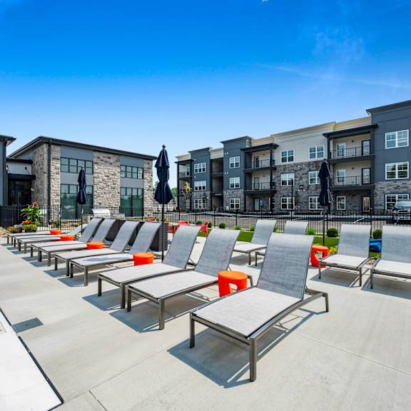 a poolside area with sun loungers and a row of apartment buildings in the background.