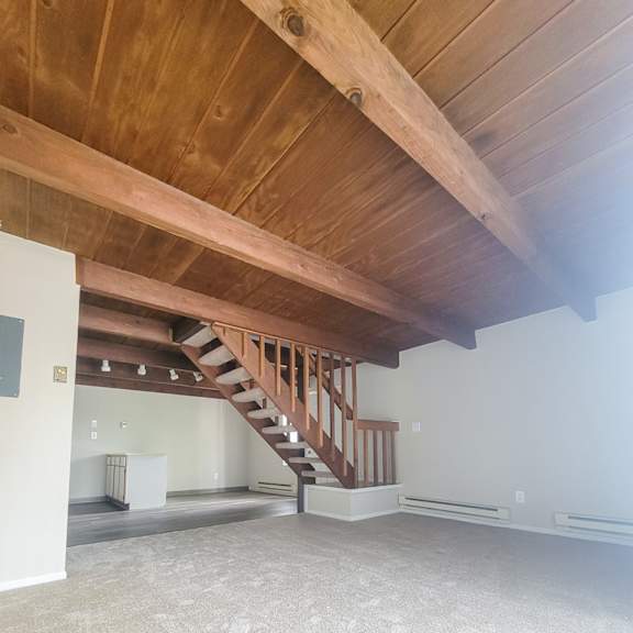 a large room with a wooden ceiling and stairs to the second floor