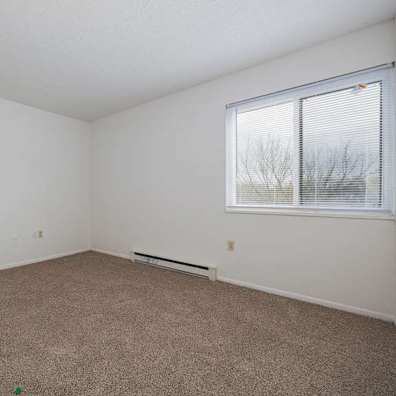 a room with a carpeted floor and a window with blinds.