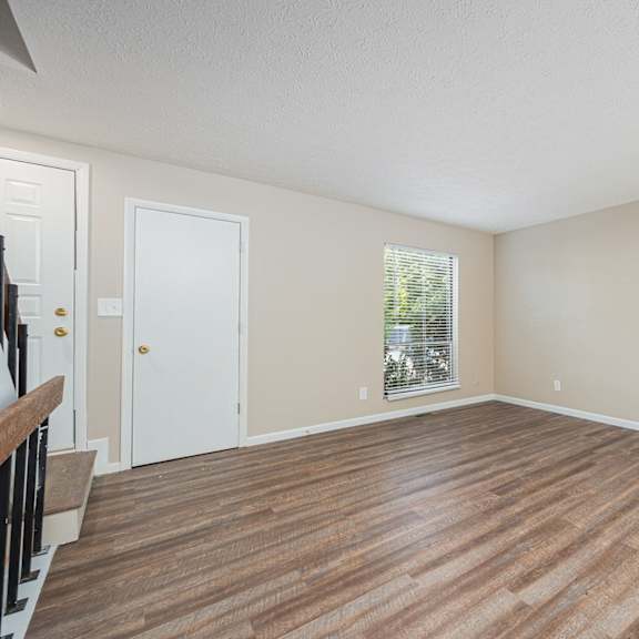 an empty living room with wood flooring and a window