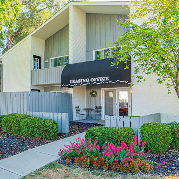 the front of a building with a leasing office sign and flowers