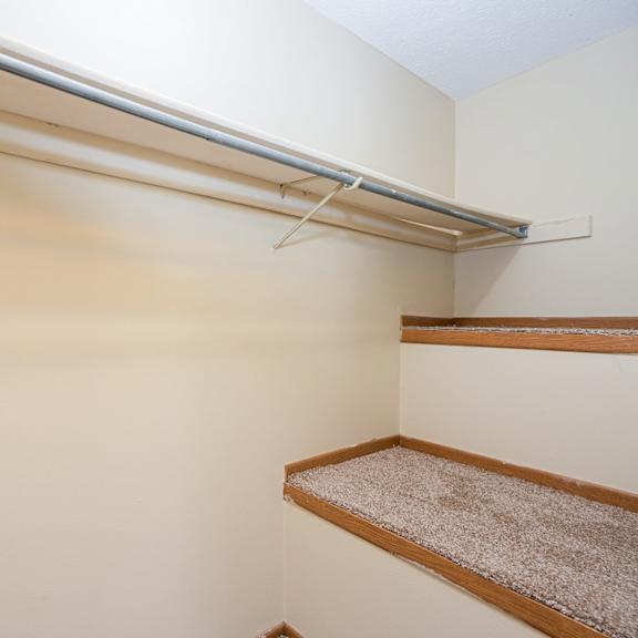 a walk in closet with a white wall and a shelf on the wall