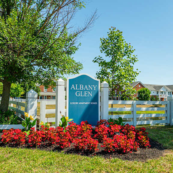 a sign for albany glen in front of a fence and red flowers