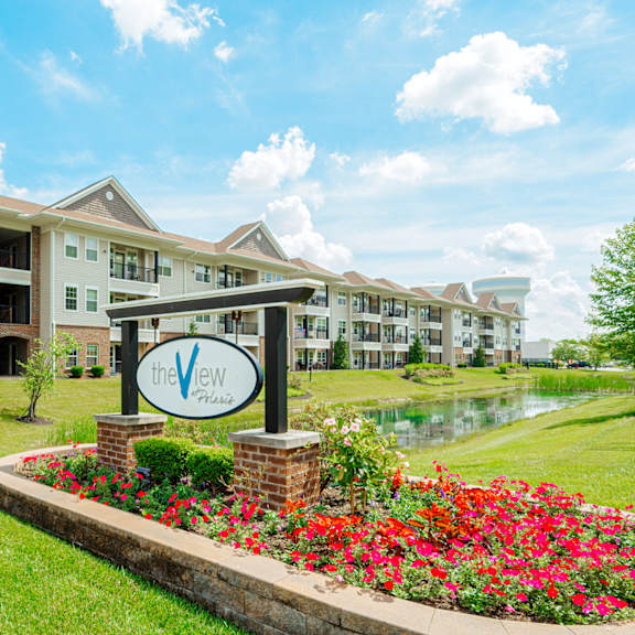 an apartment building with a sign in front of a pond and flowers