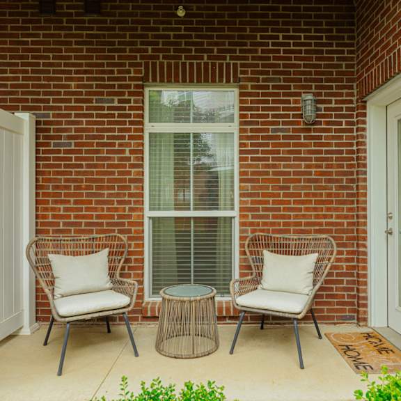 a patio with two chairs and a table in front of a brick house