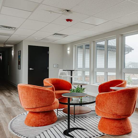 a lounge area with orange chairs and a black and white rug
