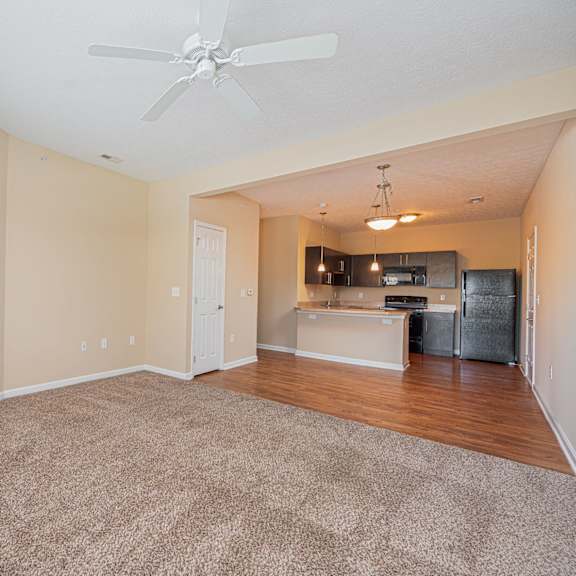 an empty living room with a ceiling fan and a kitchen