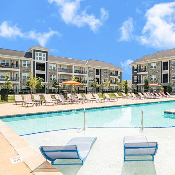 a swimming pool with lounge chairs in front of an apartment building