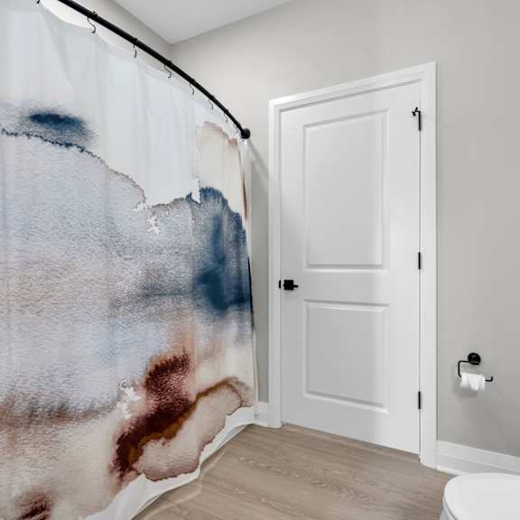 a white door is in a bathroom with a shower curtain that has blue and brown paint on it.