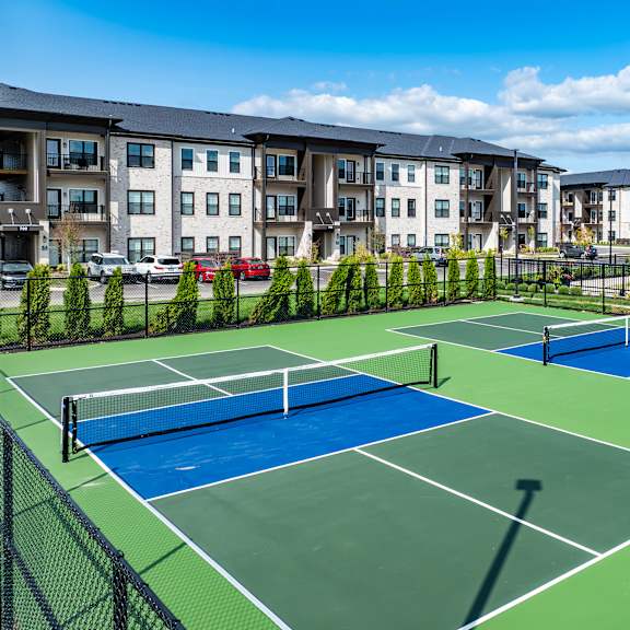 A tennis court is surrounded by apartment buildings.