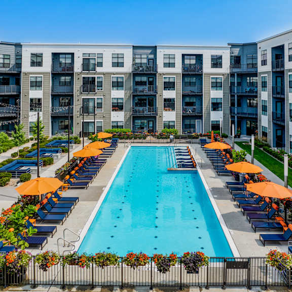 an outdoor pool with orange umbrellas in front of an apartment building