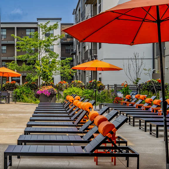 a pool with lounge chairs and umbrellas at an apartment complex