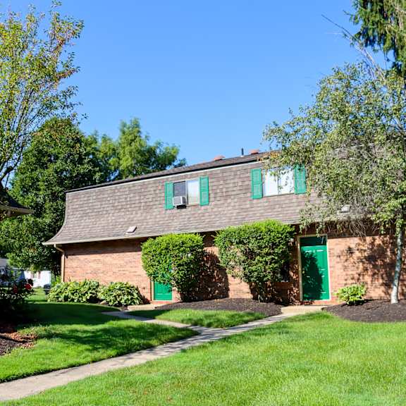 a brick house with green doors and a lawn