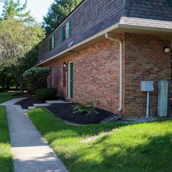 a walkway in front of a brick house with a yard and a patio