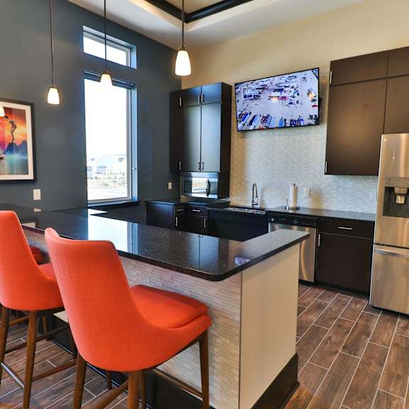 a kitchen with a bar with orange chairs and a stainless steel refrigerator