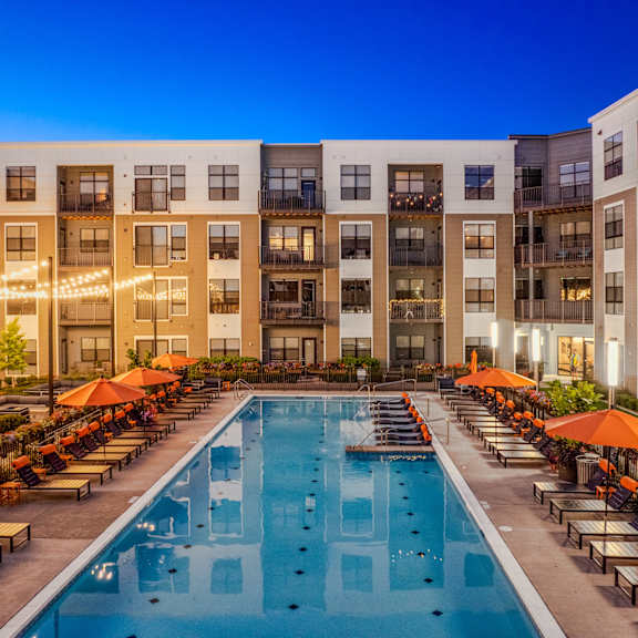 an outdoor pool with lounge chairs and umbrellas in front of an apartment building