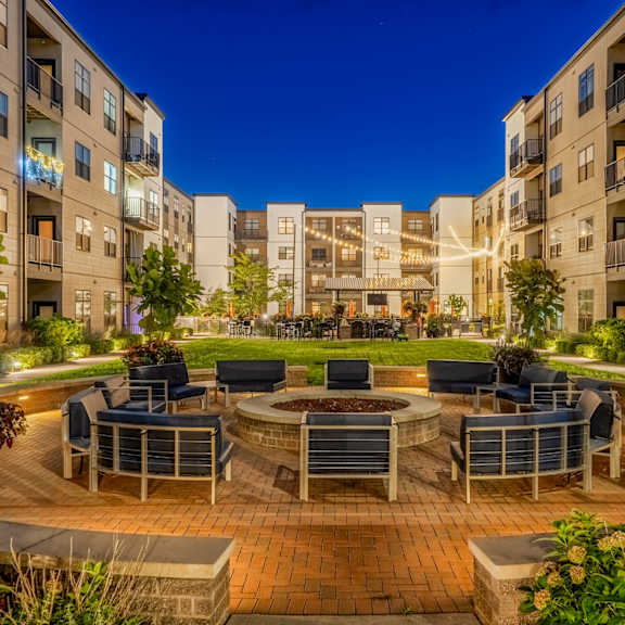 an outdoor area with a fire pit and chairs in front of an apartment building