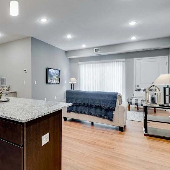 Thumbnail 3 of 12 a kitchen with an island and a living room with a couch. Circle Pines, MN Lexington Lofts