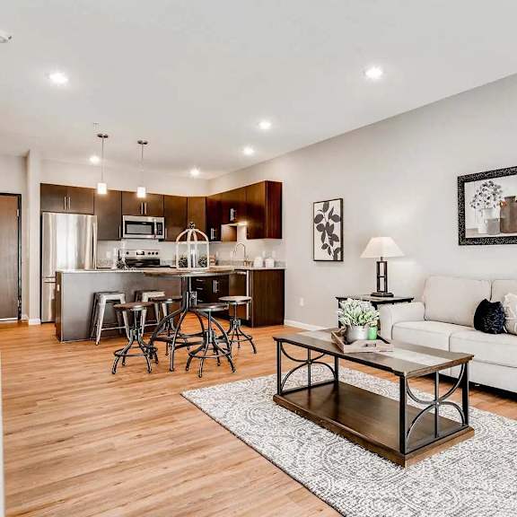 Thumbnail 6 of 9 a living room with a couch and a table in front of a kitchen. Circle Pines, MN Lexington Lofts