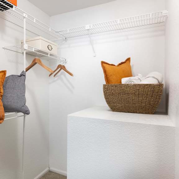 a walk in closet with pillows and a basket on a shelf in a closet