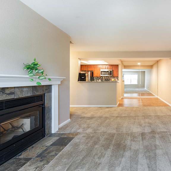 a living room with a fireplace and a hallway with a kitchen
