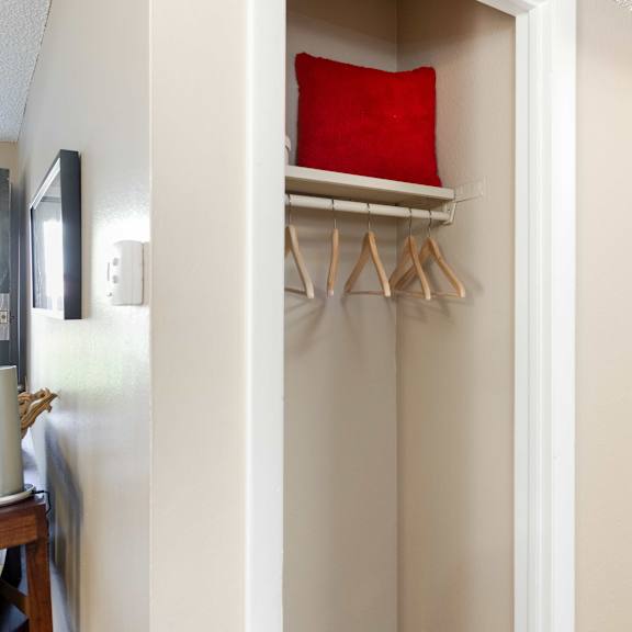 a closet with a red pillow and a white shelf with hangers