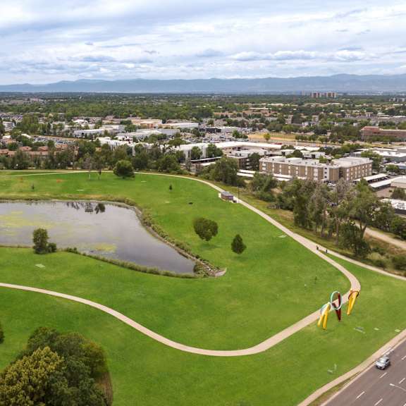 an aerial view of a park with a pond and a city in the background