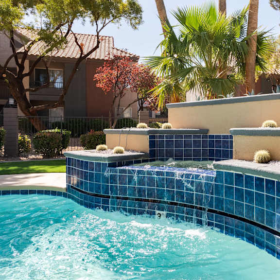 a swimming pool with a blue tiled fountain in a backyard
