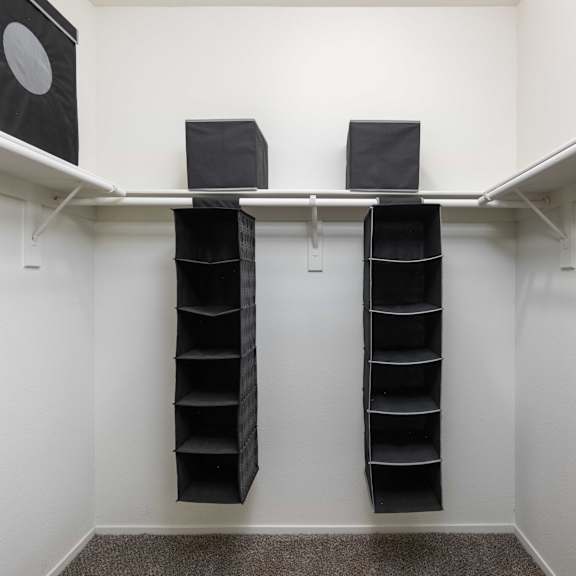 a walk in closet with black shoe racks and a white wall