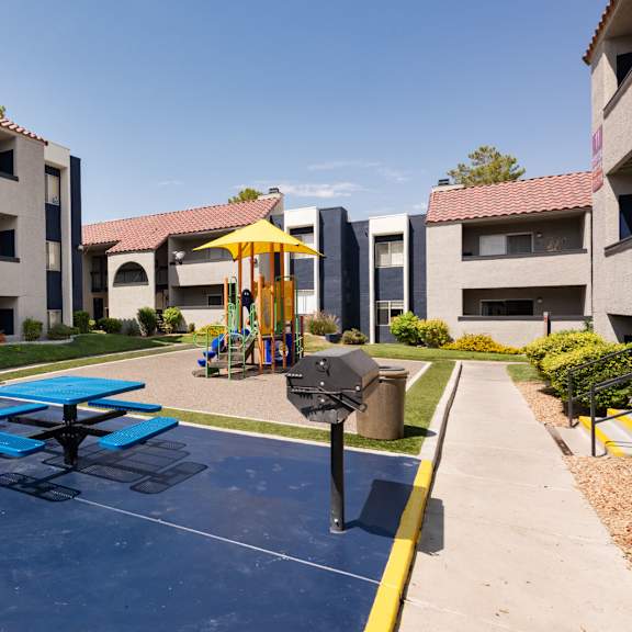 an outdoor play area with picnic tables and an umbrella